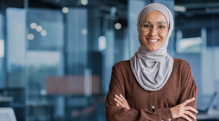 Woman in hijab with arms crossed smiling at camera