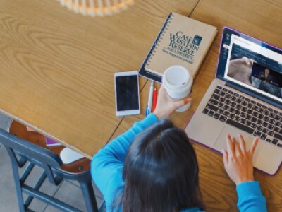 student with coffee watching a instructor video with a Case Western book