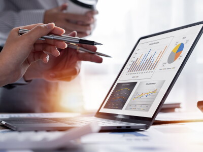 Hands of two people using pens to point at the charts on an open laptop.