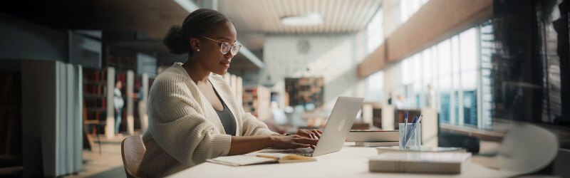 Female Student Engaged in Online Learning at a Modern Library.