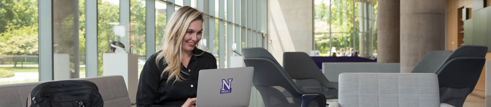 IMC graduate on laptop in the lobby of the Evanston campus
