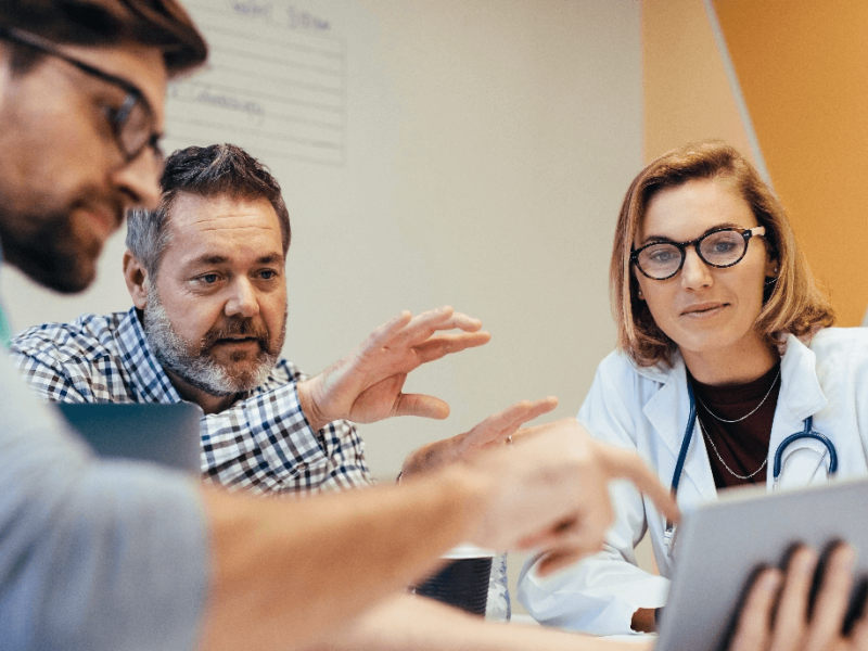 Two men and a woman in medical uniforms looking at tablet