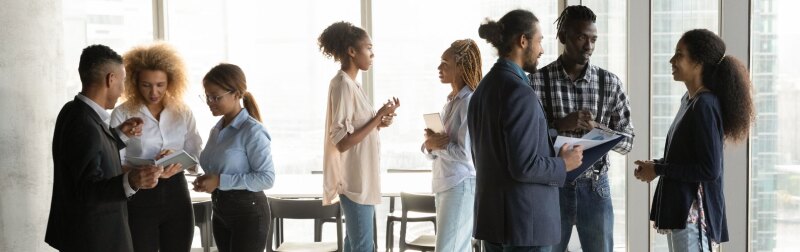 Group of young business professionals network with one another in a corner meeting room.