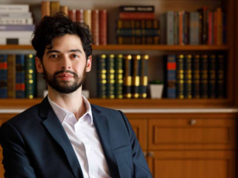 man looking at the camera in front of a full bookcase