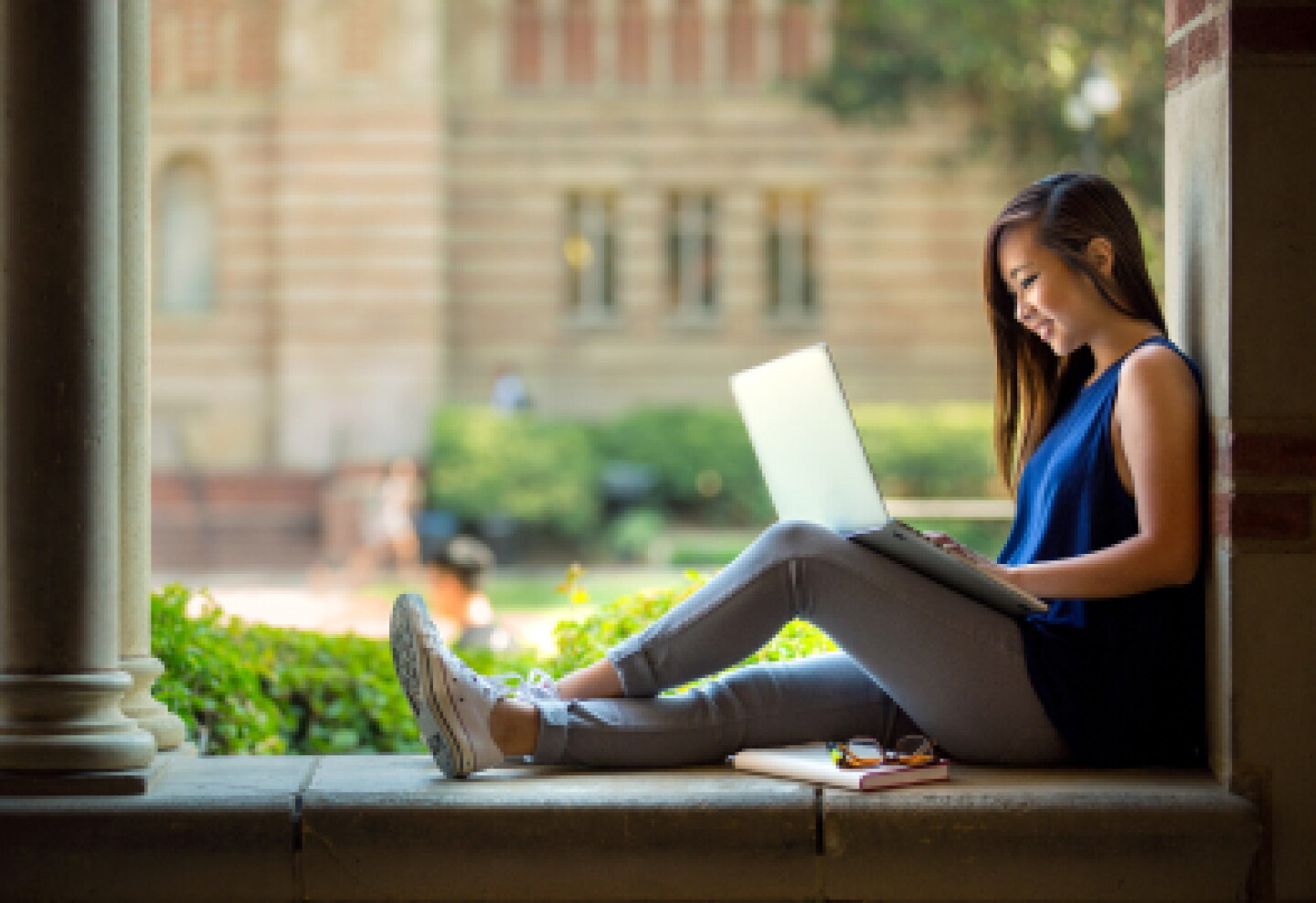 A female CWRU student sitting in a library window while working on online lessons.