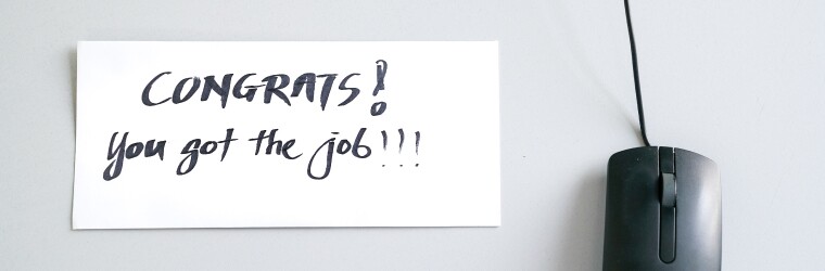 Sticky note on a desk next to mouse reads "congrats! you got the job!"
