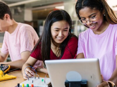Diverse teenage students building electronic circuits in a high school lab.