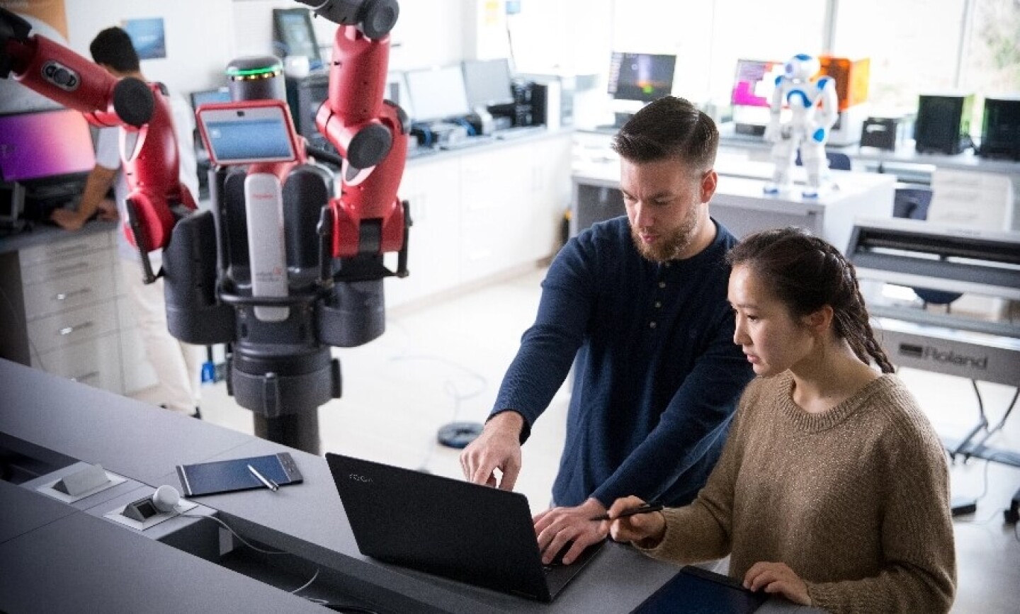 Male and female student working with robotic arm and laptop computer