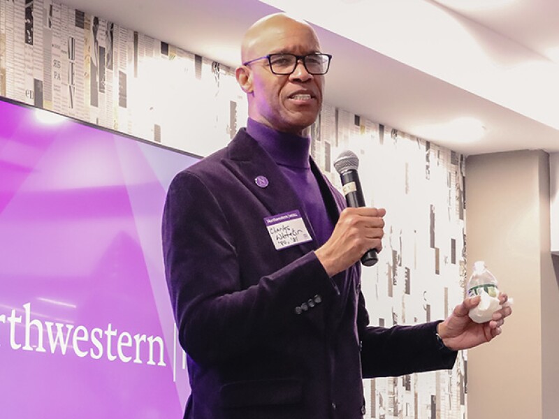 Man in blazer speaking in front of Northwestern sign