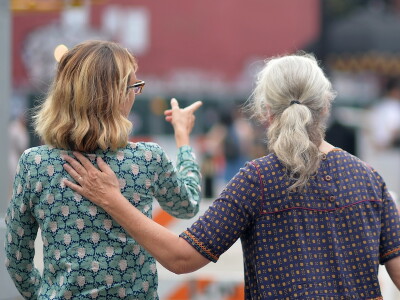 Two women walk together through a New York City neighborhood, talking as one gestures ahead.