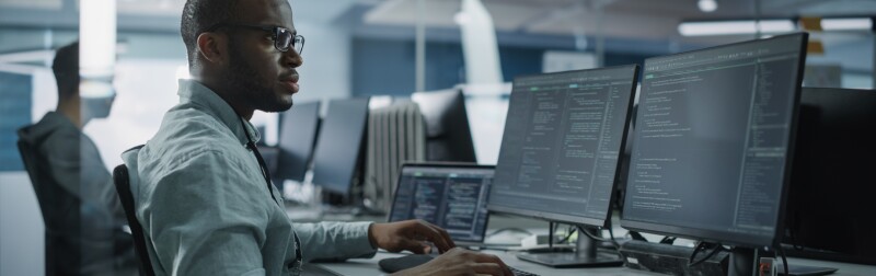 Male Software Engineer Developing App on a multi-monitor computer.