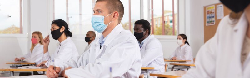 Focused man studying in classroom with medical colleagues in protective face masks for disease prevention during training program.
