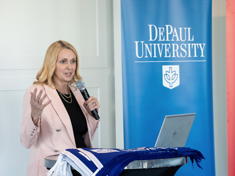 woman speaking into microphone in front of DePaul University banner