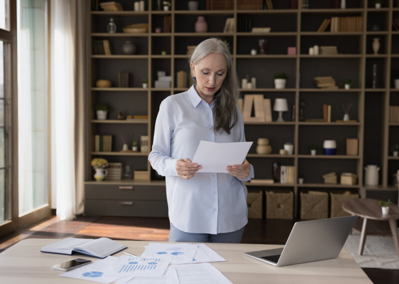 Woman stands in front of desk at home office reviewing a document