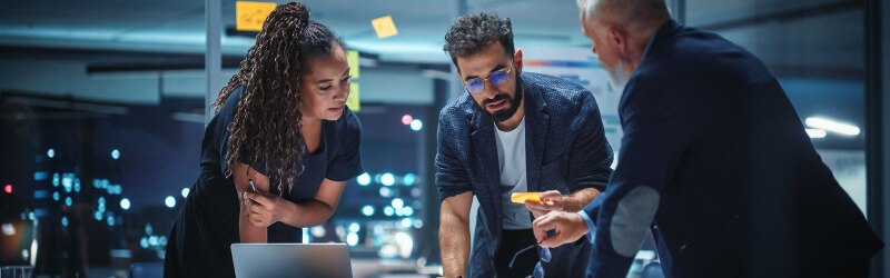 A diverse team of marketing managers talk, brainstorm, and use a computer to make creative decisions.