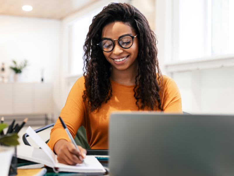 Woman using laptop and writing in notebook