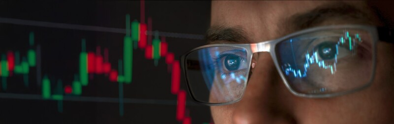 A close-up view of a man wearing glasses, with data charts reflecting on the lenses