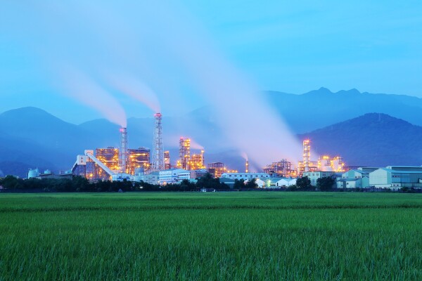 View of a factory in the middle of a green farmland in the early morning twilight ~ Factory pipes polluting air in a silent morning, a serious environmental issue