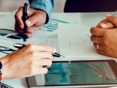 Hands of three people collaborating at a table over graphs and tablet