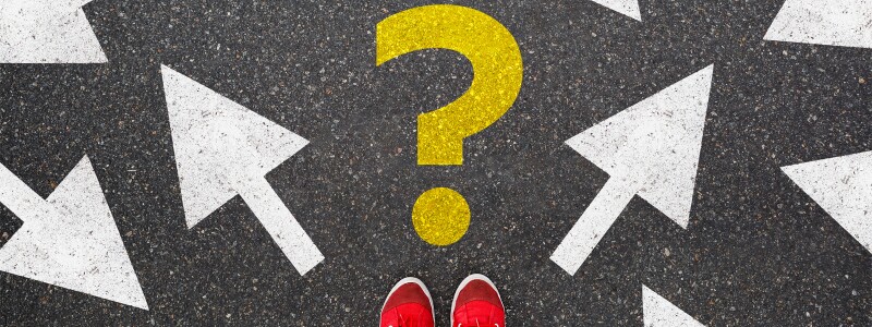 A yellow question mark painted on the ground surround by arrows pointing in various directions