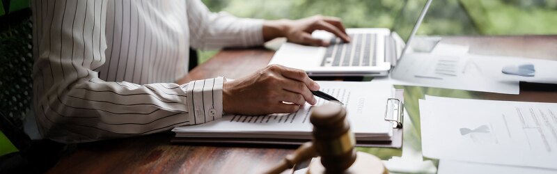 a person sitting at a desk with a laptop and clipboard next to a gavel