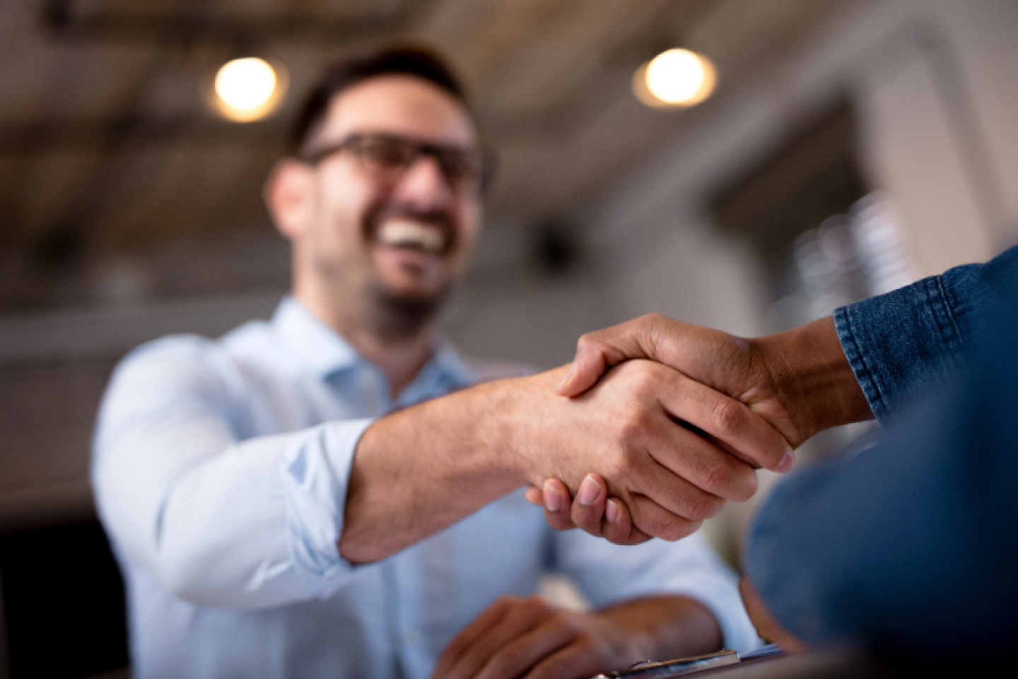 Close-up of two people shaking hands, with one person smiling in the background, representing a successful business agreement or partnership.