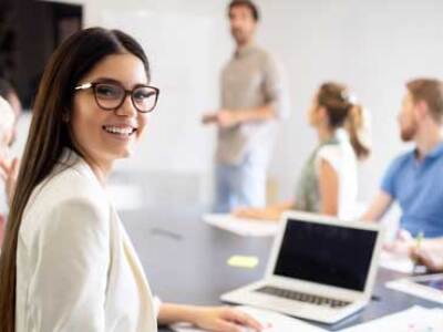 Smiling student in class, seated at a laptop