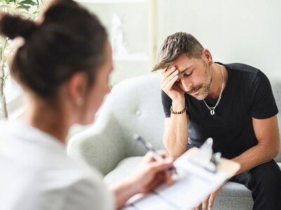 male client sitting on couch with head in hand while counselor takes notes