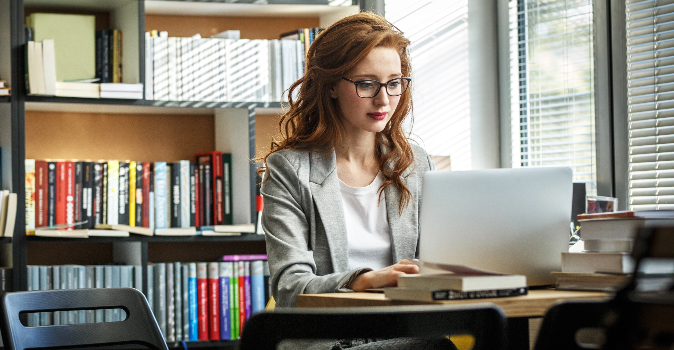Female educator sitting at a workspace, surrounded by books and her laptop, reviewing documents