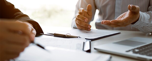 close up image of two sets of hands over paperwork and a laptop