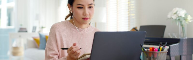 Asian female student wearing earphone while listening to digital online course development program.