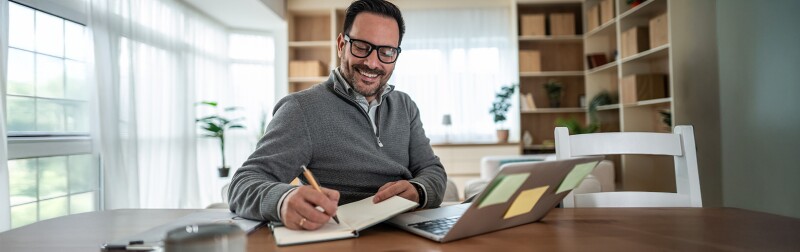 Man writing notes while working on his laptop from home