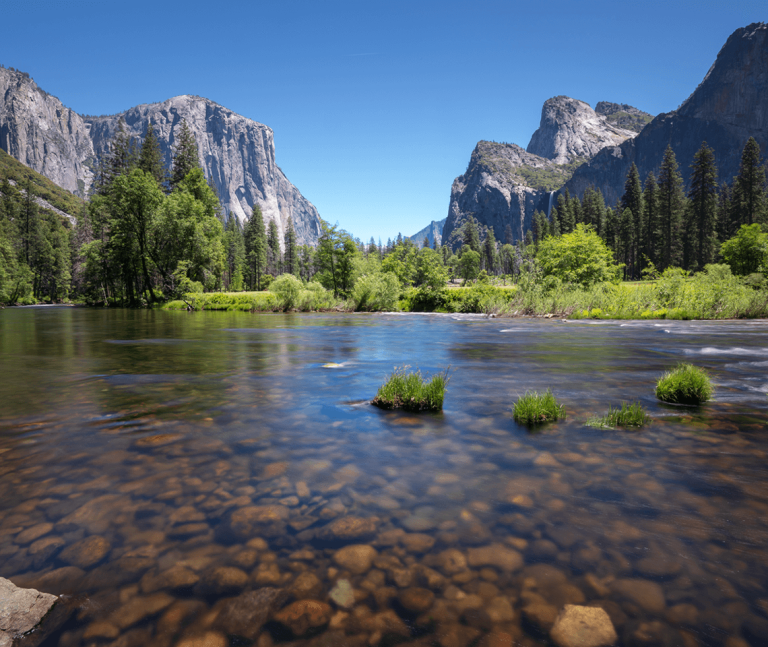 A river flowing through a mountainous area with trees and blue skies