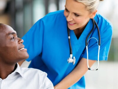 Successful healthcare professional pushing her wheel-chaired patient down the hospital hallway.