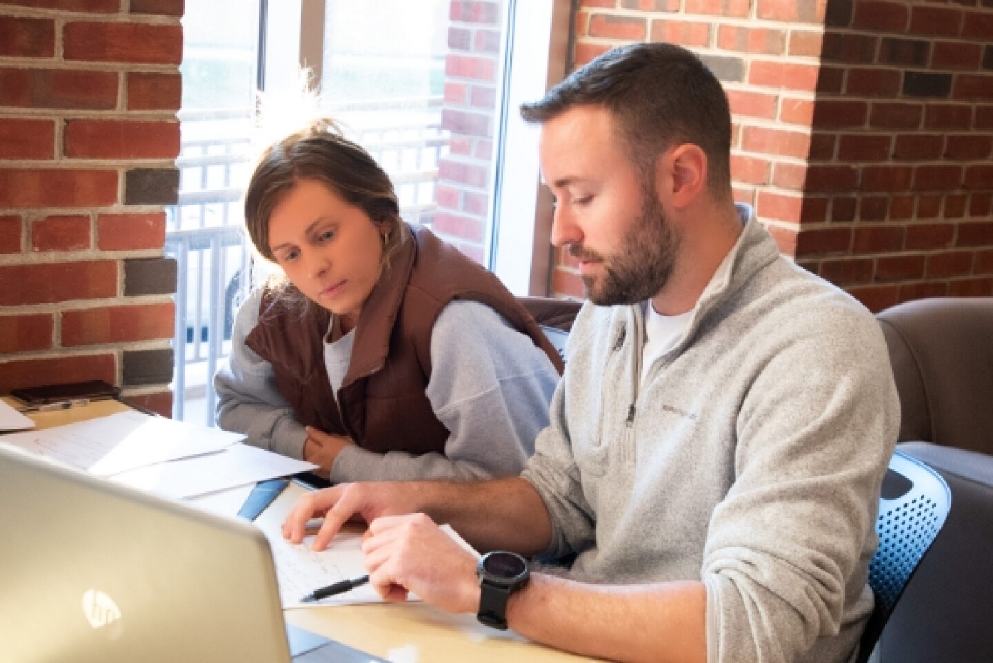 Two students collaborating over papers and laptop at desk