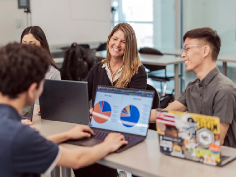 A female CSUMB student smiles while having conversation with fellow students at table.