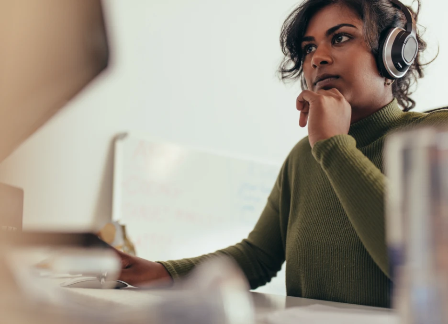 Woman wearing headphones contemplates project at desk