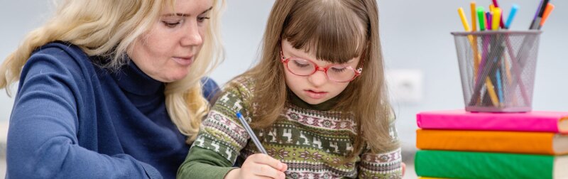 Young girl with Down Syndrome works with her teacher in the classroom.