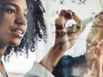 Two female business professionals in collaboration for business strategy on glass board.