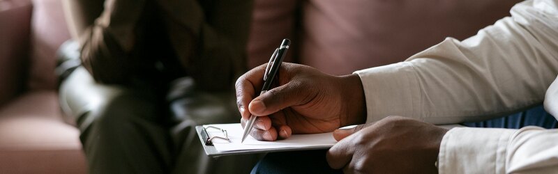counselor wearing long sleeve white shirt taking notes on clipboard