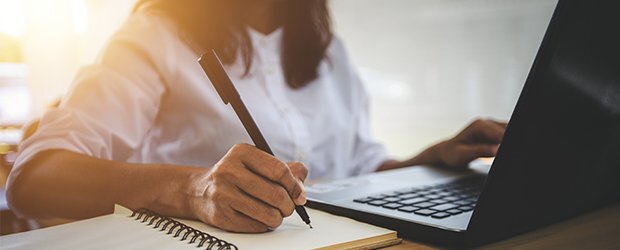 woman-writing-in-notebook-on-laptop-backlit