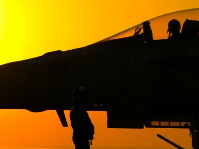 Silhouette of military personnel and a fighter jet against a vibrant sunset, representing aviation and military operations.
