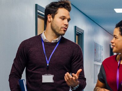 Two teachers are walking down a school hallway discussing teaching plans.