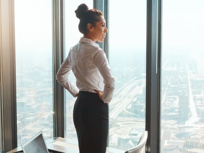 Woman standing in front of windows in a skyscraper with hands are on her hips admiring the view.