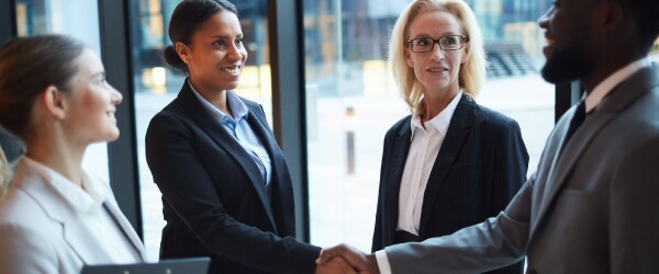 Two people shake hands in a group of diverse professionals