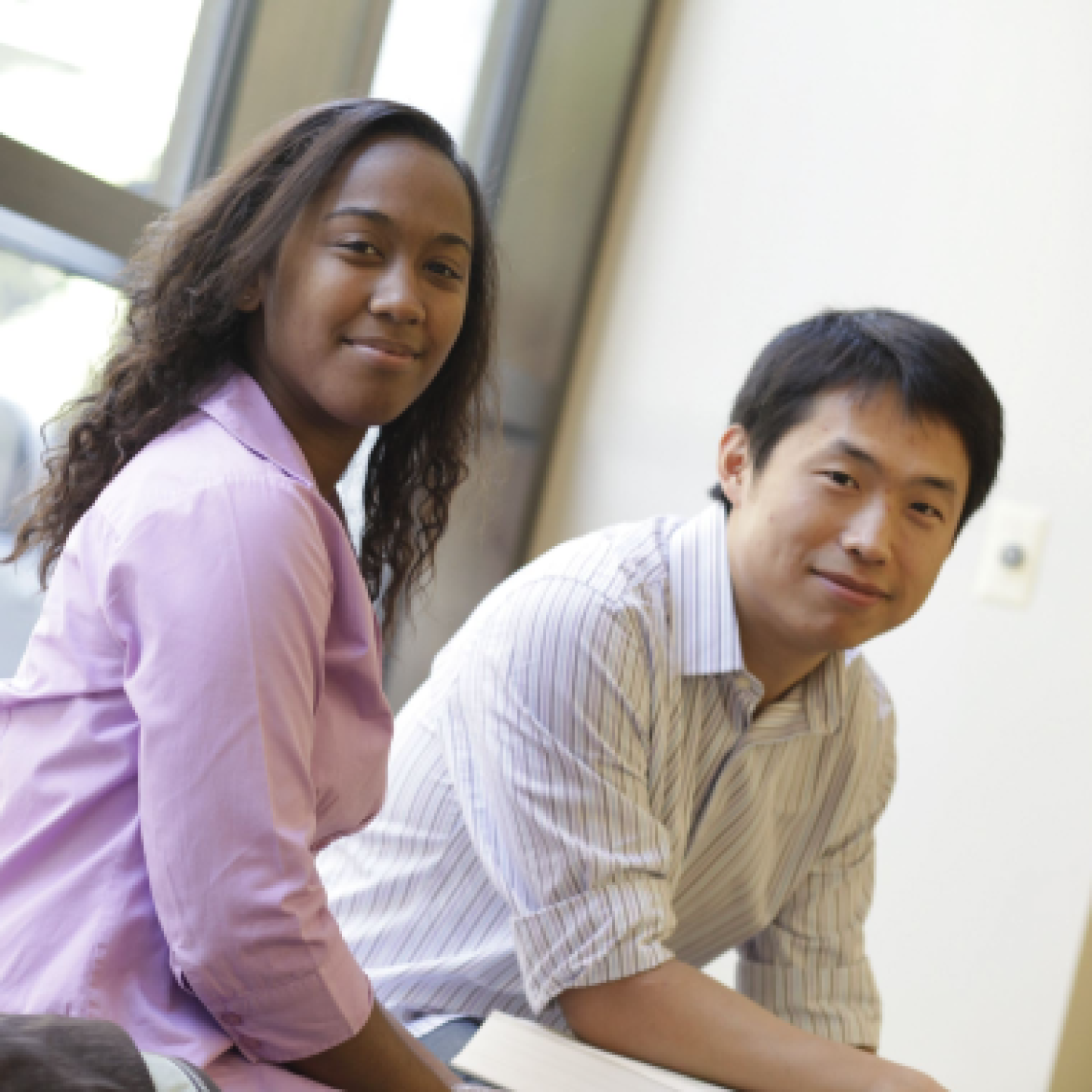 An asian male and a black female Yeshiva University students sitting next to a window.