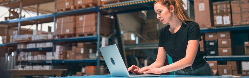 Female warehouse manager using laptop to review shipping data.