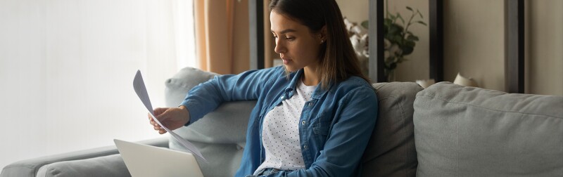 Woman sitting on a couch with laptop and looking over paperwork