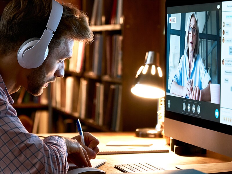 Man listening to professor speak in online class while taking notes