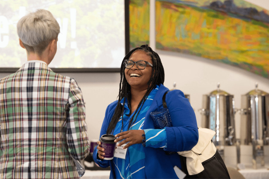 Woman in blue coat holding coffee and laughing with Tulane professor